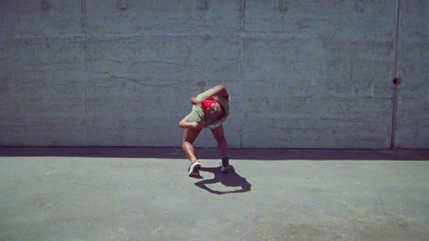 Woman energetically dancing in front a concrete wall