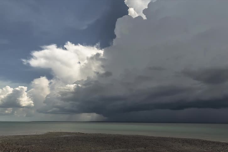 Dark clouds move in over cumulus clouds along the shoreline