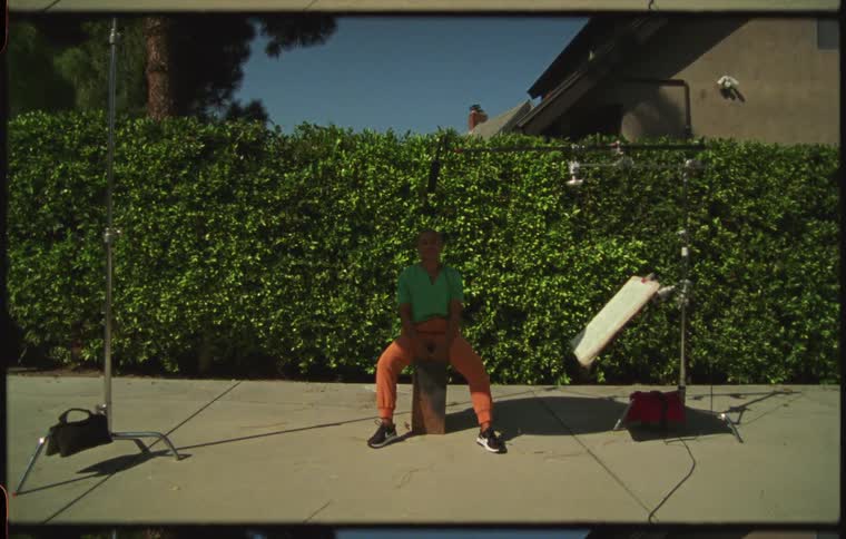 Woman sitting on the sidewalk in front of a bush surrounde by photography equipmnet