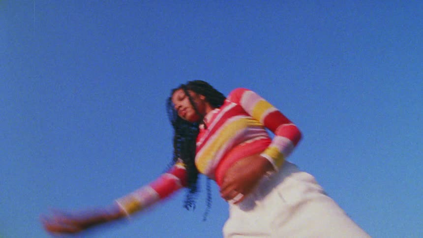 Young long haired woman energetically dancing in front of a clear blue sky