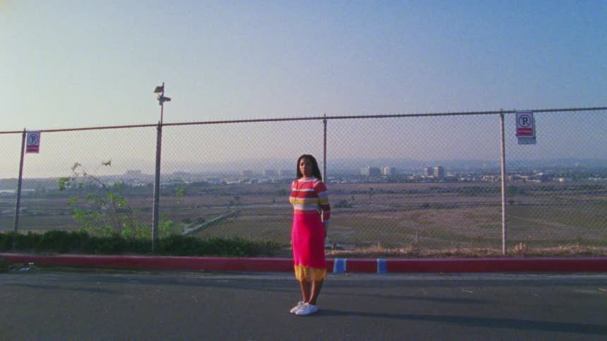 Woman stands on road near fence with city on background