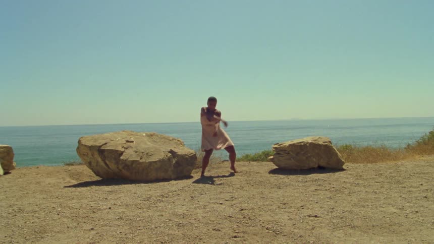 A woman performs a dance routine in the sunshine overlooking the ocean