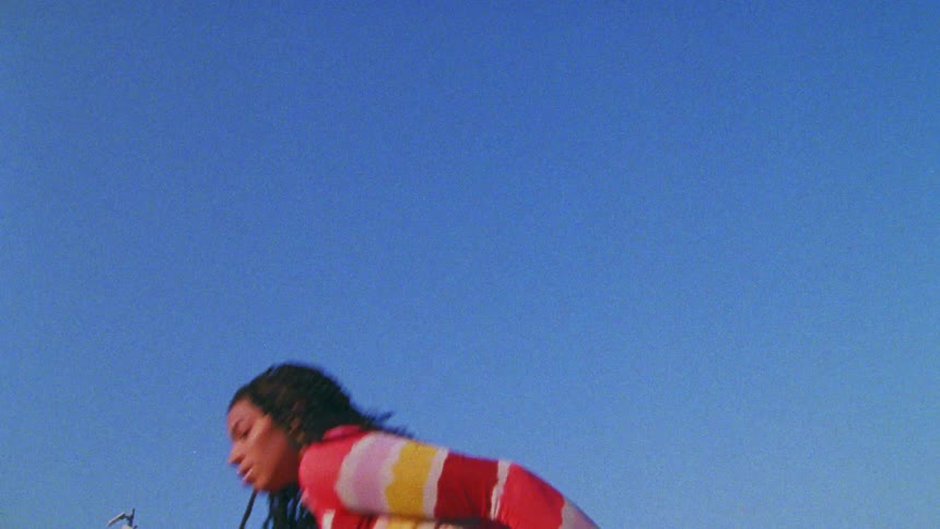 A young woman dances outdoors under a clear blue daytime sky
