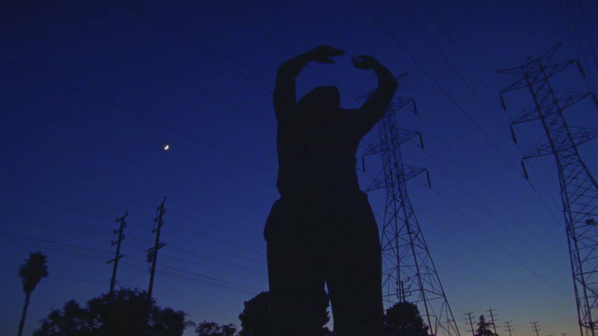 Silhouette of a woman dancing near transmission towers under the moon at night