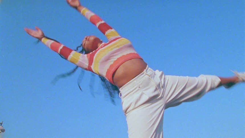 A young long haired woman energetically dancing in front of a clear blue sky
