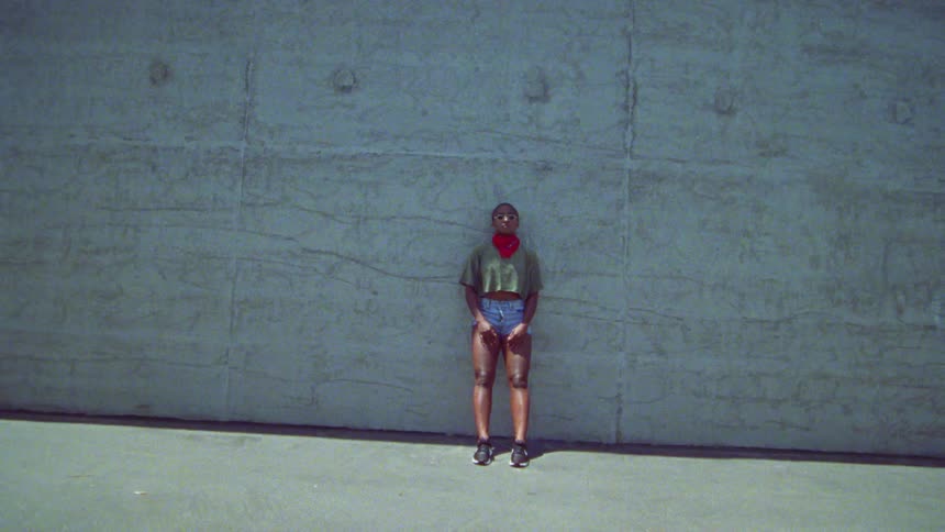Woman standing outside leaning against a large concrete wall in a pose