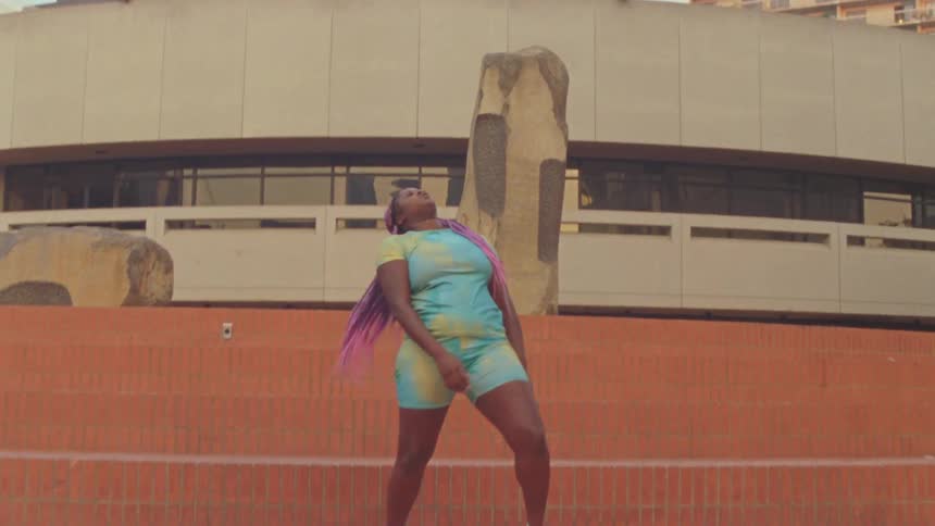 Young woman with long pink hair dances in front of a building in the city