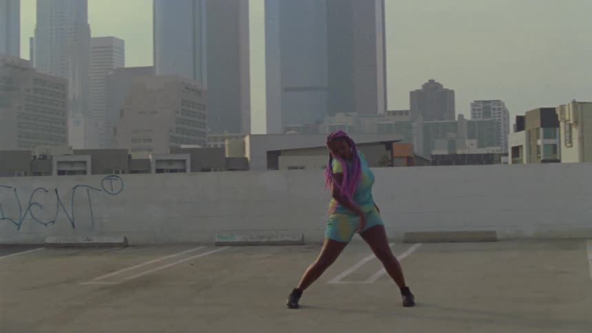 A woman dances in an empty lot on the top of a parking garage in a metropolis during the day