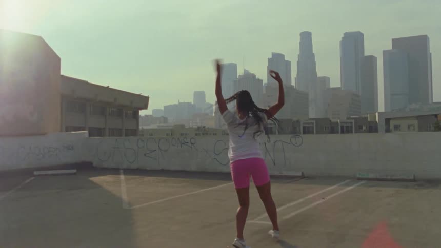 A woman dancing on a rooftop parking lot in a city at daytime