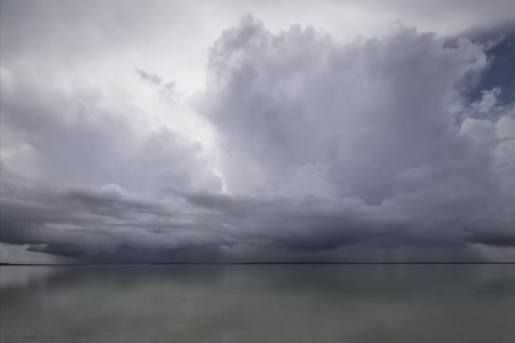 Cumulus clouds above an ocean move across the sky on a very cloudy day