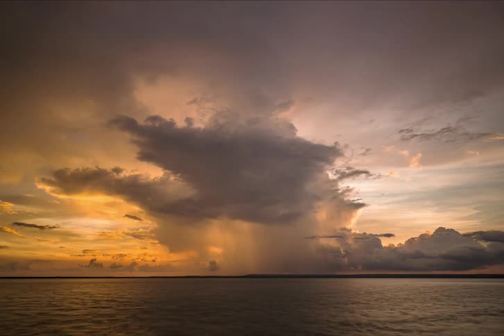 Clouds move across an ocean as the sky turns orange