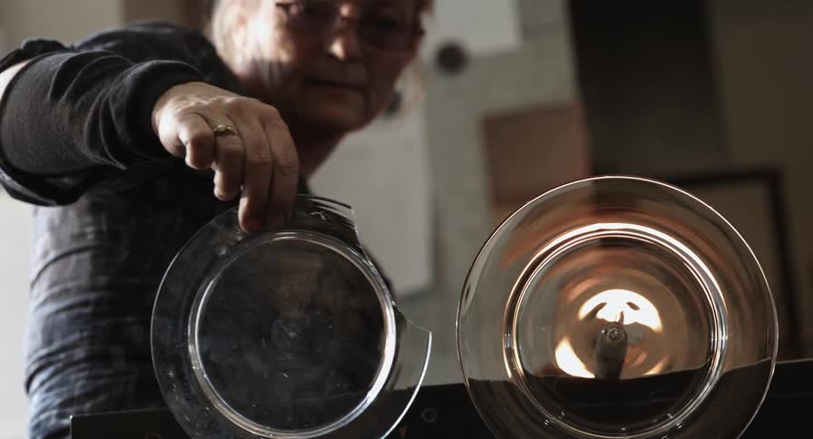 A woman holds up a broken plate next to a glass blown plate