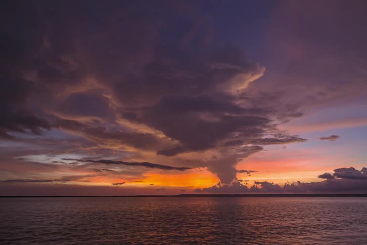 A body of water with waves rippling with the sky and clouds in the background