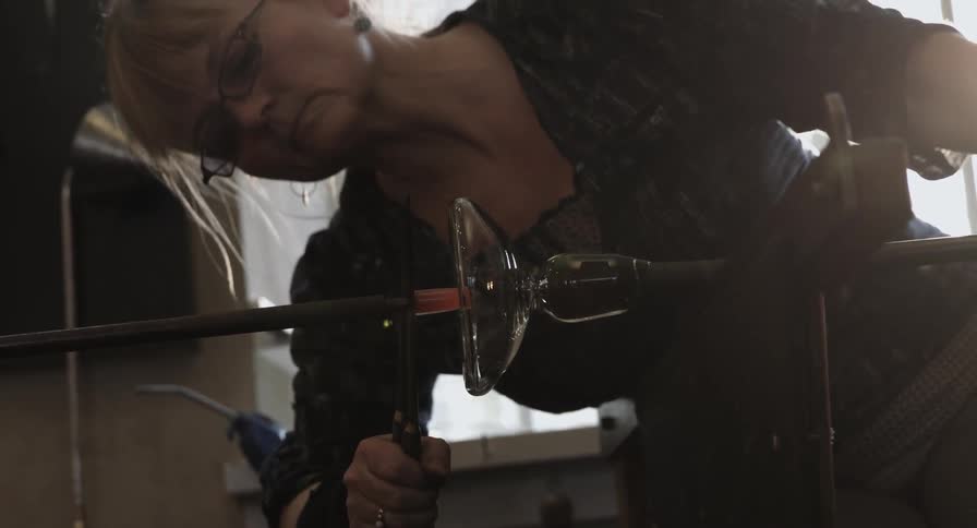 A female glass artisan crafts the bottom of a glass piece