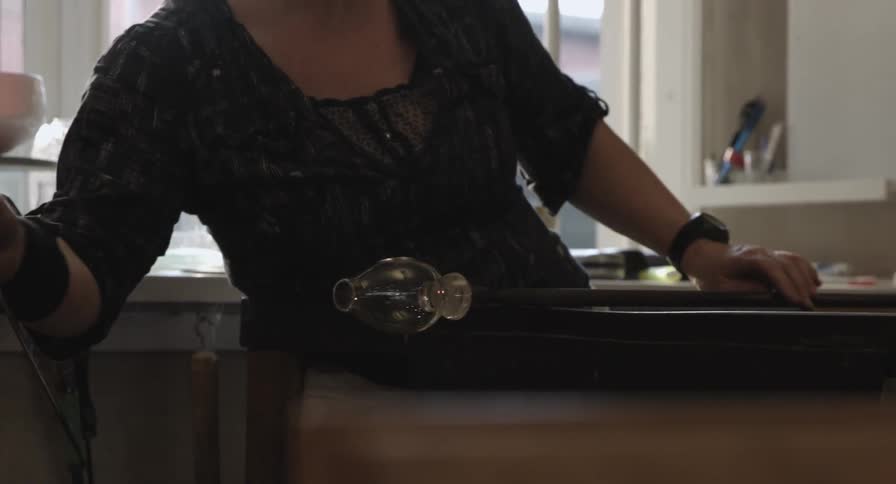 A woman molds and rolls a piece of glass while it is still hot