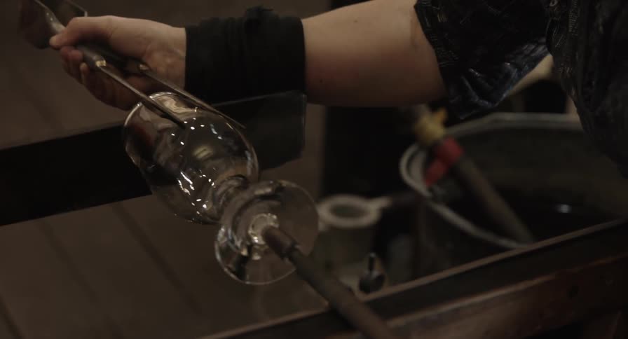 A woman using an instrument to mold a piece of glass