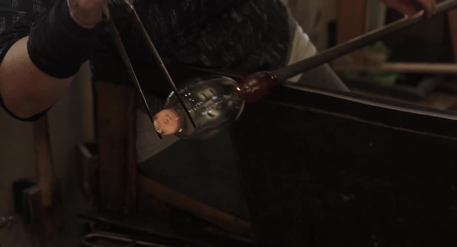 An artisan works a hot ball of glass into a shape