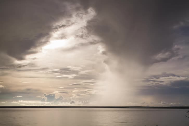 Cloud formation flows low over ocean stretching to land on horizon