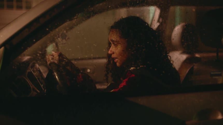 A woman in a vehicle holding on to the steering wheel with raindrops on the window