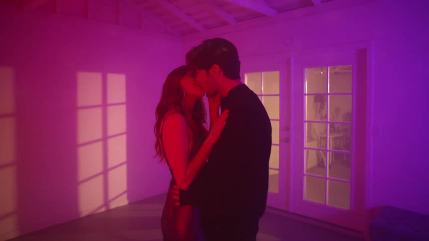 A man and woman kiss under a disco ball in a mostly empty room at home