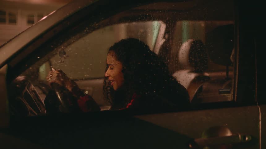 A woman sitting in a vehicle holding the steering wheel and crying with water drops on the window