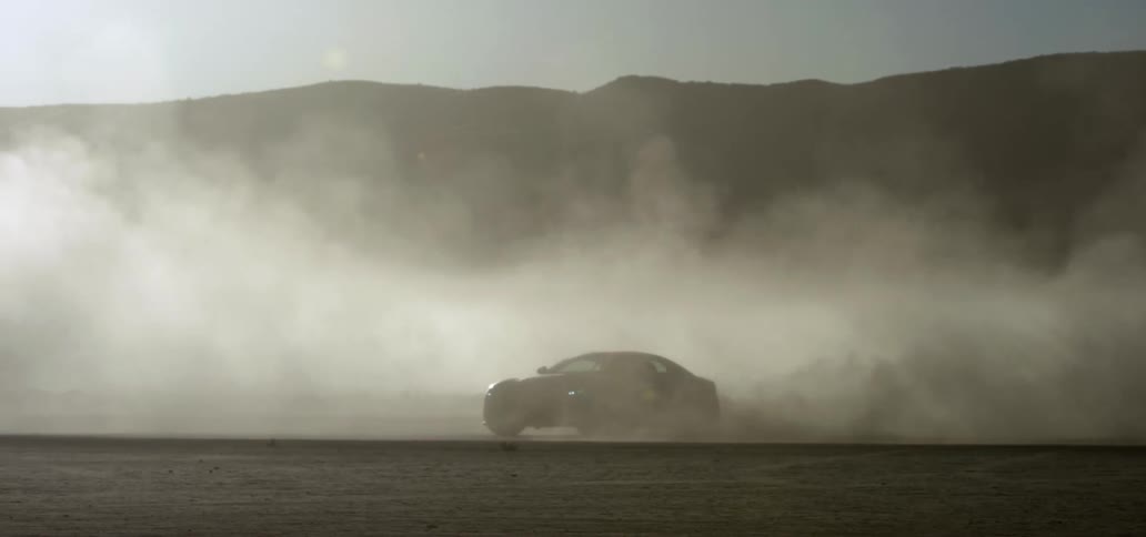 A black sports car drifting in dirt in a desert driving through haze at daytime