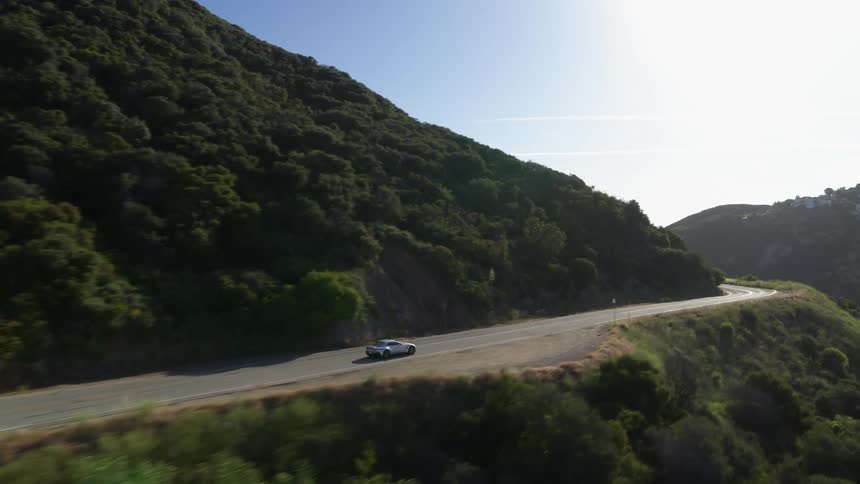 A car travels a road on a large tree covered mountain