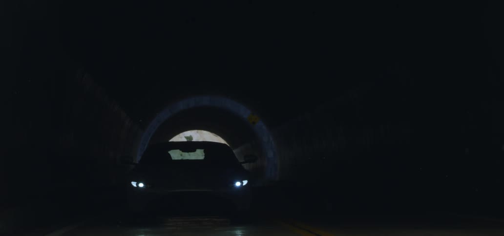 A coupe sports car driving out of a tunnel with headlights on