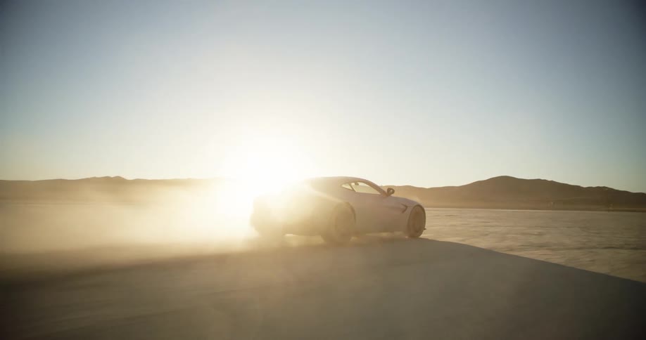 Sports car leaving a dust trail while driving on the desert at sunset