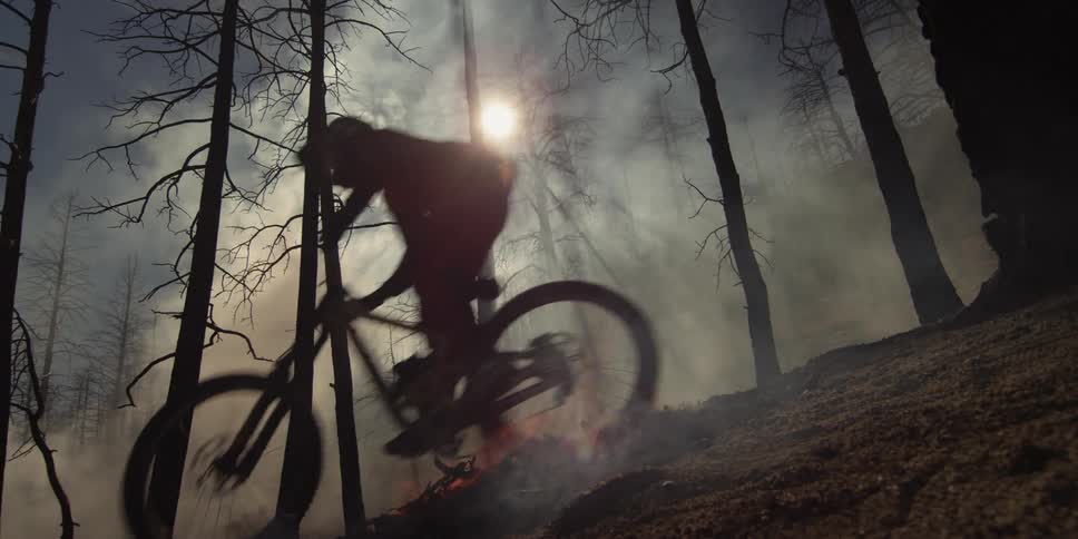 A person rides their mountain bike down a hill past a burning fire