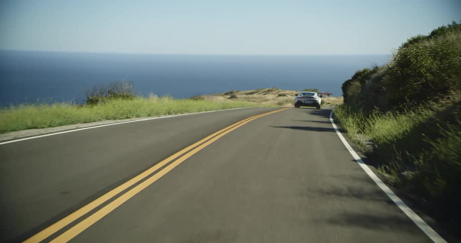 A silver luxury vehicle drives down a highway on the side of a mountain next to a cliff at daytime