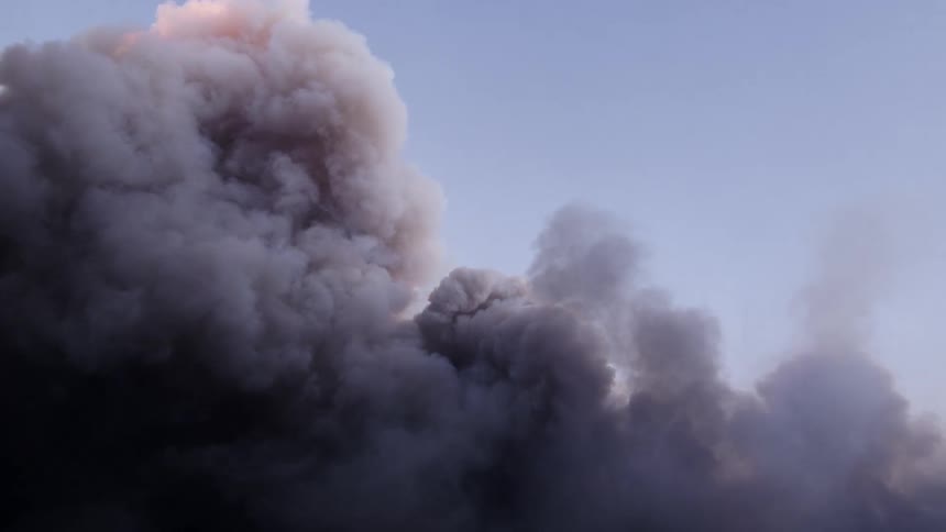 Smoke clouds rise and move across the sky