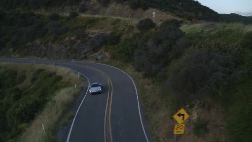 A sports car travels along a winding pass on a verdant mountain on a clear day