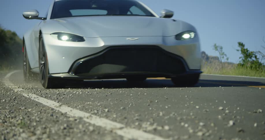 A car drives on the road and kicks a bunch of pebbles up in the air
