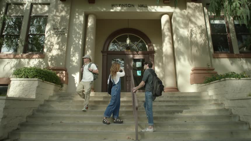 A woman stand on the steps to a college and a man walks up to her