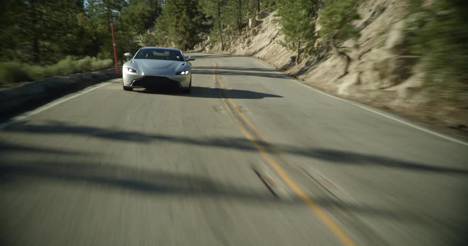 A car driving on a winding road surrounded by trees with the sky and clouds in the background