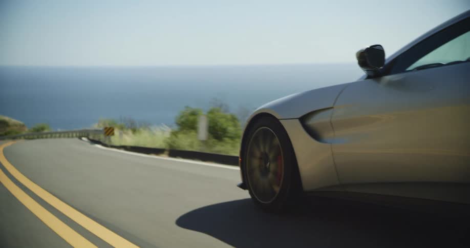 Coupe sports car driving on a road in the mountains near the ocean