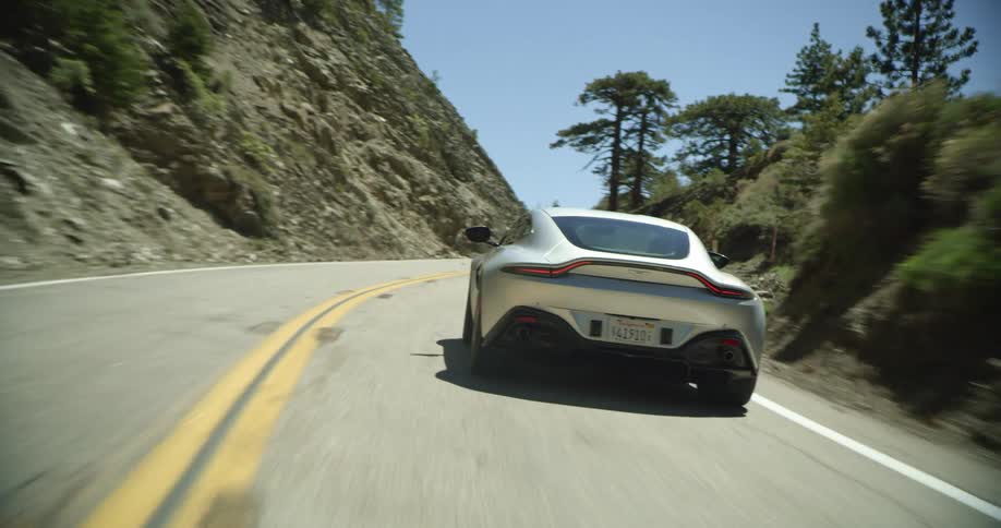Sports car drives along winding road past forest and mountain slopes