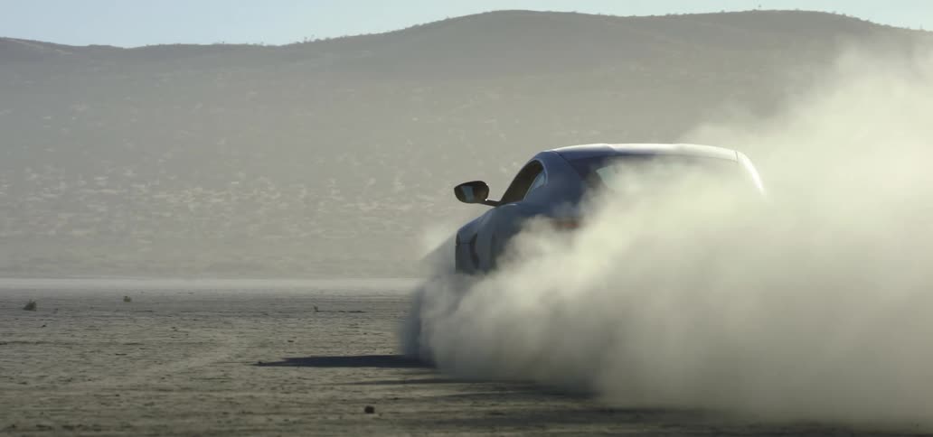 Dust billows behind a car as it drives across the dirt terrain