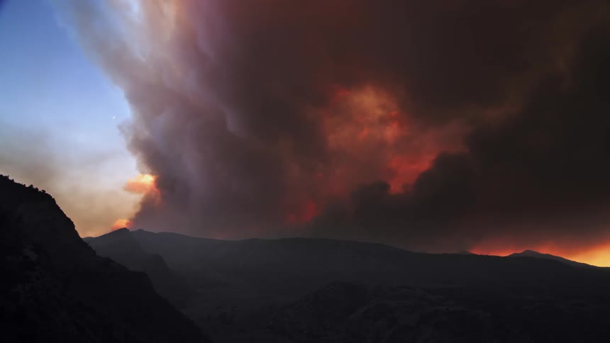 A massive wildfire engulfing a mountain in the horizon