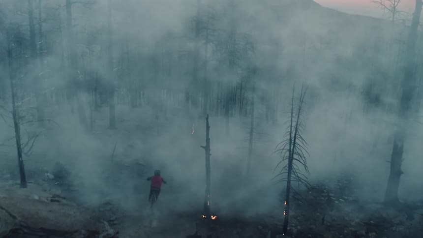 A person rides mountain bike through burning forest and disappears into smoke.
