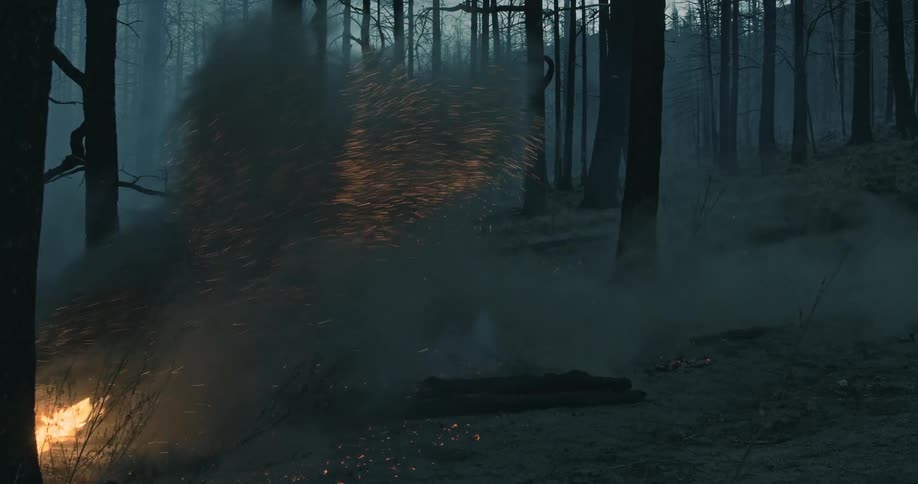 A person on a bike riding over a bonfire kicking up an ash cloud.