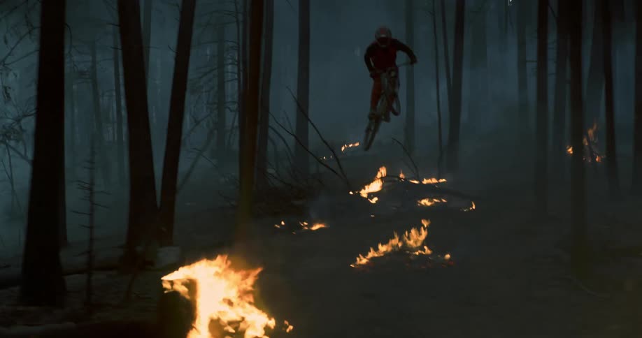A person rides a mountain bike over flames in a forest fire fast.