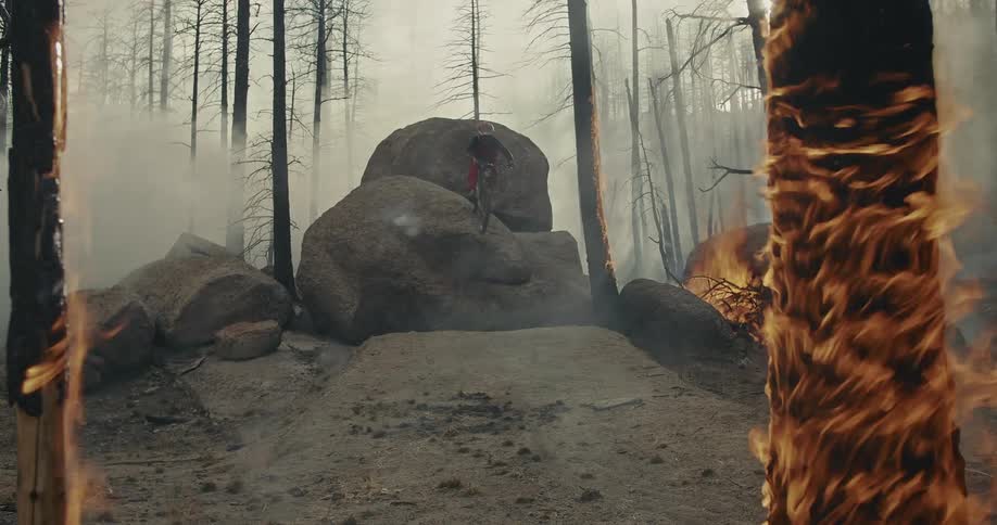 Cyclist jumps a mountain bike over on to a rock in the ashes of a burning forest