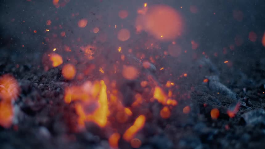 Embers explode upward from center of charred burnt coal