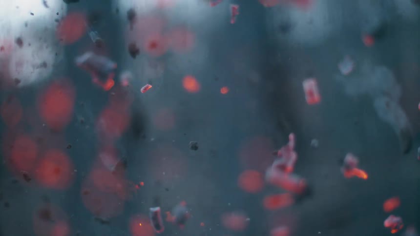 A blast of black and red embers emerge from the ground and scatter about in the air