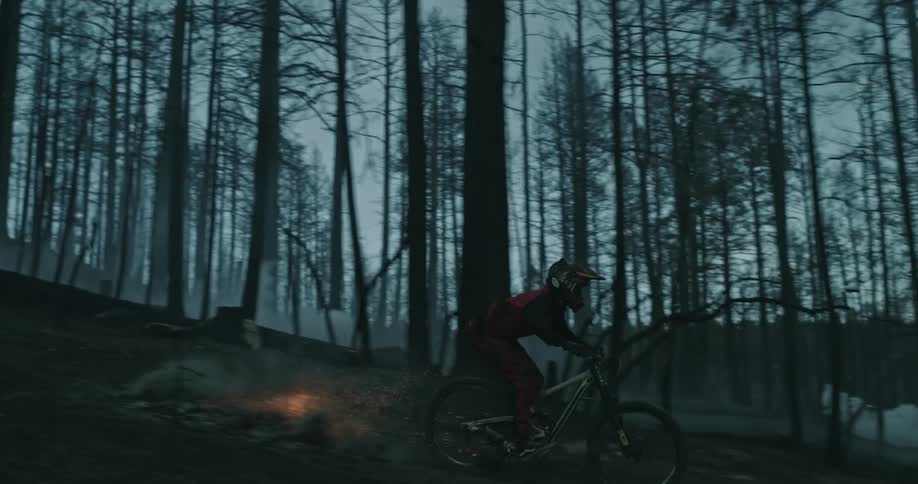 A person rides a mountain bike down burning logs in a dark forest.