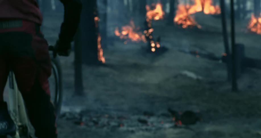 A man on a bike leaps through a forest that is on fire
