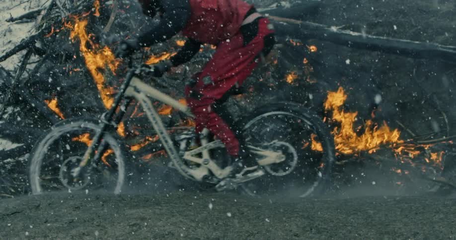 Cyclist wall rides a mountain bike in the raining ashes on a burning forest