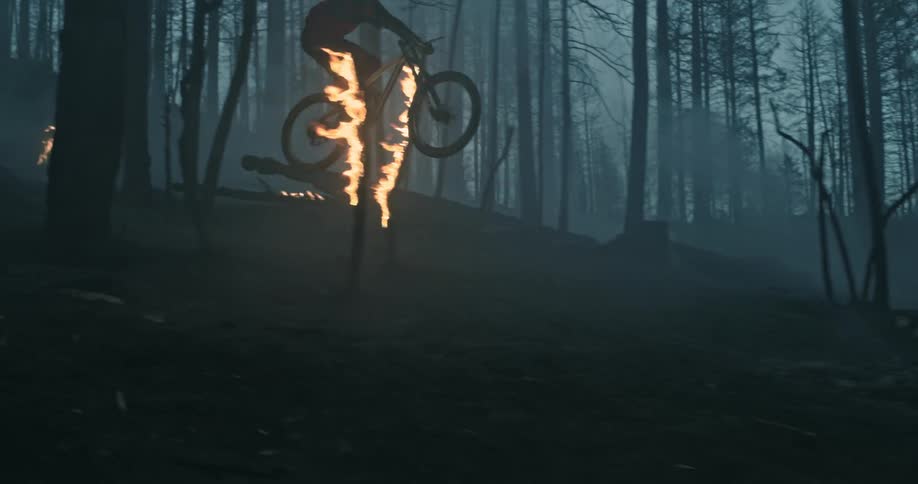 A person wearing a helmet and riding a mountain bike leaps in the air riding through a forest fire